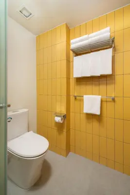 a bathroom with a toilet and a yellow tiled wall at lyf Malate Manila managed by The Ascott Limited in Manila