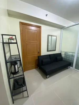 a living room with a black couch and a wooden door at Sea Residences MOA by Ruffa's Condotel in Manila