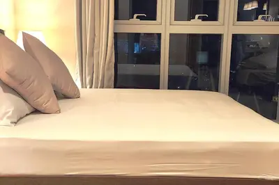 a bed with white sheets and pillows next to a window at Casa Antonio At Uptown Parksuites Two in Manila
