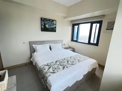 a bedroom with a bed with white sheets and a window at Partial Ocean View Opposite the US Embassy in Manila