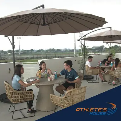 a group of people sitting at tables under an umbrella at Athlete's House in Imus
