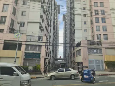 two cars driving down a city street with tall buildings at 1 Bedroom Condo In Little Baguio Terraces, San Juan City in Manila