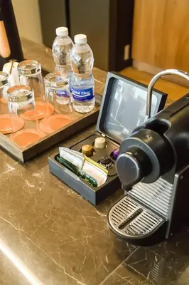 a coffee maker on a counter with glasses and water bottles at Brittany Hotel Villar City in Cavite