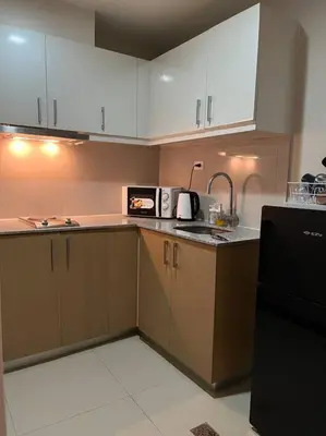 a kitchen with white cabinets and a black microwave at BGC Uptown Mall Suite in Manila