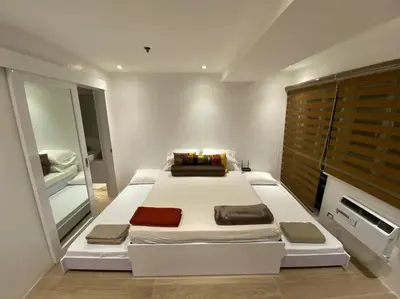 a bedroom with a large white bed and a mirror at Cozy60sqm 1BR balcony/prking/Wifi/Ntflix near Mall in Manila