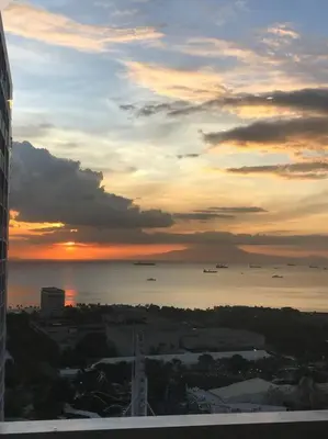 a sunset over a city with the ocean and a building at Breeze Residences with Ocean view by Bmars in Manila