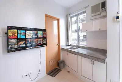 a kitchen with white cabinets and a tv on the wall at JP Santiago Studio Makati J206 in Manila