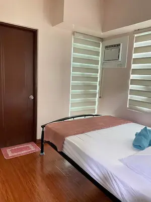 a bedroom with a bed with white sheets and windows at Anuva Residence Condominium in Manila