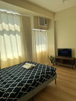 a bedroom with a bed and a tv and a window at Neat Unit in Holland Park Southwoods in Biñan