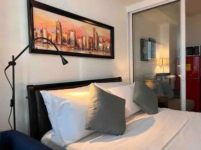 a bedroom with a white bed with a painting on the wall at Relaxing 1-Bedroom Unit in Azure Urban Resort and Residences by One Guest Place in Manila