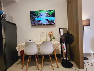 a dining room table with three white chairs and a tv on the wall at Fame Residences Staycation in Manila