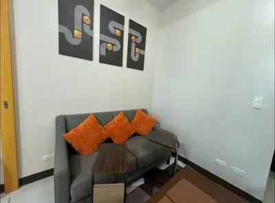 a living room with a gray couch with orange pillows at Modish 1BR One Uptown BGC direct to Uptown Mall in Manila
