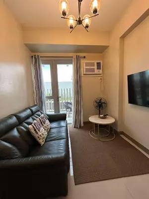 a living room with a black leather couch and a tv at The Verdin at Maple Grove in Cavite