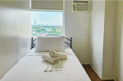 a bed with towels and slippers on it with a window at Homes by Gilmore Tower Suites in Manila
