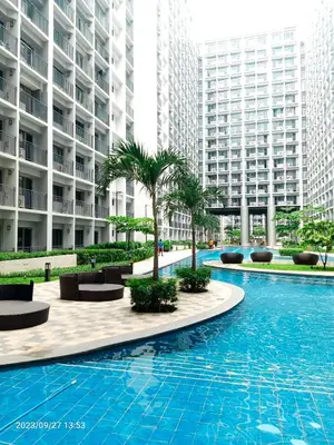 a large swimming pool with palm trees and buildings at Shore 2 Residences 1BR Deluxe Room in MOA Complex in Manila