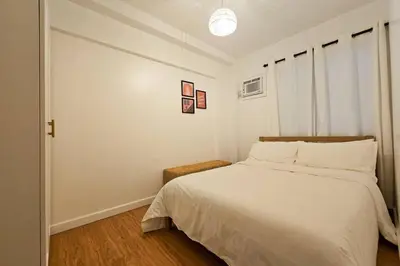 a bedroom with a bed with white sheets and a window at Bohemian Inspired 2 Bedroom Inspired Condo with Fast WIFI Near BGC in Manila