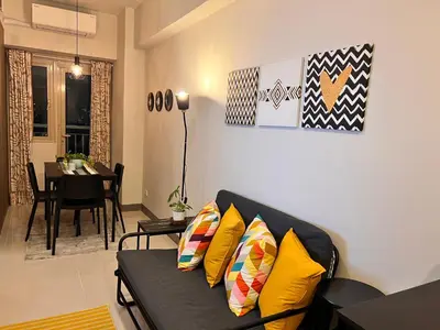 a living room with a black couch with yellow pillows at CozyCoastStay by APPLETRAVELBEYONDPH in Manila