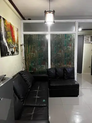 a living room with a black leather couch in front of a window at V&J Transient Condotel in Manila