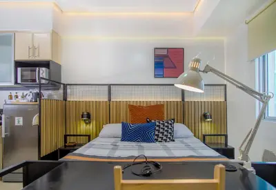 a bedroom with a bed with a desk and a lamp at Relaxing Apt Bgc Business Ready with 84inch Cinema in Manila