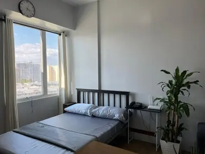 a bedroom with a bed and a window with a clock at Studio Getaway in Alabang at Anuva Residences in Manila