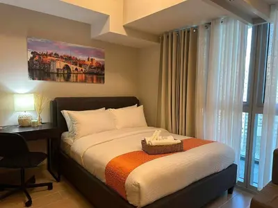 a bedroom with a bed and a desk and a window at Cozy Pad BGC in Manila