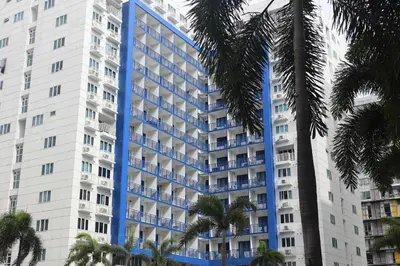 a tall white building with blue windows and a palm tree at Sea Residences Yeshua infront of MOA Pasay in Manila