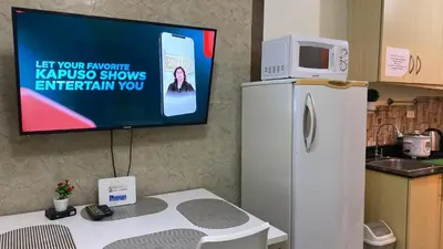 a tv on a wall next to a kitchen with a refrigerator at CHATEAU ELYSEE A16 Near Resto And Sm Mall/Airport in Manila