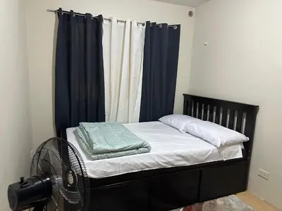 a bedroom with a bed with blue curtains and a fan at B-G Sorento Oasis 2BR in Manila