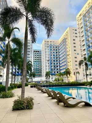 a resort with a pool and palm trees and buildings at Sea Residences: Eyal’s Suite Condotel near MOA/Mall of Asia in Manila