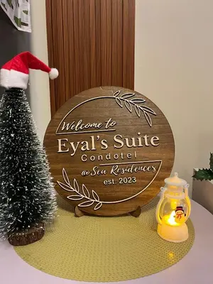 a christmas sign on a table with a christmas tree at Sea Residences: Eyal’s Suite Condotel near MOA/Mall of Asia in Manila