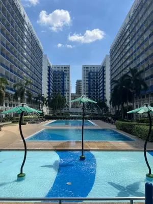 a swimming pool with two umbrellas in a city at 2BR Staycation in front of MOA Near Aiports Entertainment City Ayala Malls Parqal Worldtrade Center PICC Starcity SEA ESCAPE BLISS in Manila