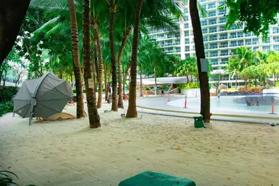 a beach with an umbrella and palm trees and a building at Cozy Chic Condotel Azure Urban Resort Residences in Manila
