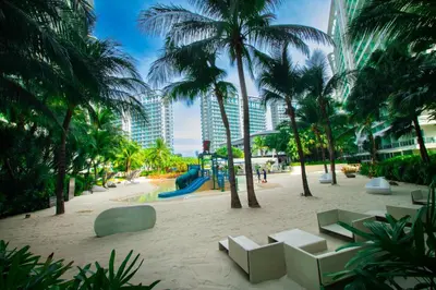 a park with palm trees and a playground with chairs at Cozy Chic Condotel Azure Urban Resort Residences in Manila