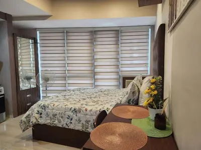 a bedroom with a bed and two tables in front of a window at KL Tower Cosy Studio with Balcony Sauna Gym Pool near Greenbelt in Manila
