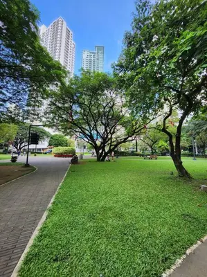 a park with trees and green grass and buildings at KL Tower Cosy Studio with Balcony Sauna Gym Pool near Greenbelt in Manila
