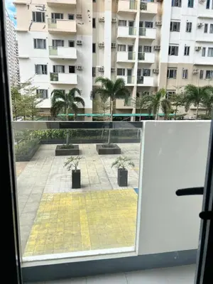 a window with a view of a courtyard with palm trees at Brand New Studio w/ Washer in Manhattan Plaza Tower ll in Manila