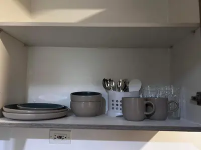 a shelf with plates and utensils on it at Connie's Fame Residence City Haven in Manila