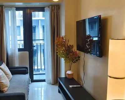 a living room with a couch and a tv on a wall at ndulge in opulence on a budget near MOA! Luxuriate in our Deluxe 1 Bedroom Units with stunning views. Enjoy free NETFLIX and an exceptional discount. Book now for a lavish and affordable escape! in Manila