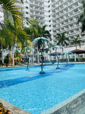 a large swimming pool with palm trees and buildings at Aiza's Place in Shell Residences MOA in Manila