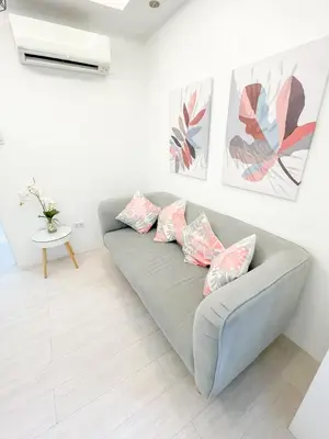 a living room with a gray couch with pink pillows at Travelers Inn - Modern Capsule Bunks, Makati in Manila
