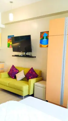 a living room with a yellow couch and a flat screen tv at Studio-Type Condo at Eastwood Legrand 3 in Manila