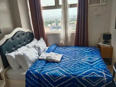 a bed with a blue comforter and a window at Pierrecondotel in Manila