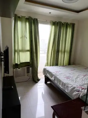 a bedroom with a bed and a window with green curtains at Birchtower studio in Manila