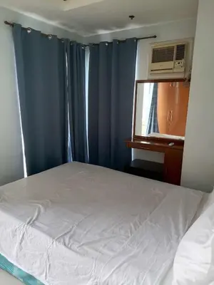 a bedroom with a bed with blue curtains and a window at Birchtower studio in Manila