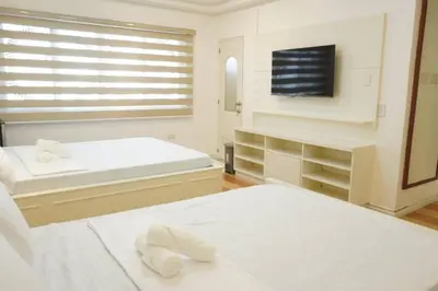 a white bedroom with two beds and a flat screen tv at Makati Altean Apartment (Leonora Room) in Manila