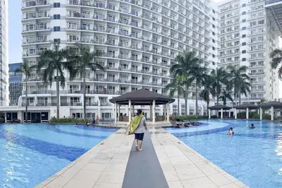 a woman standing next to a swimming pool with an umbrella at Pasay City MOA, Pearl Suite in Shell Residences in Manila