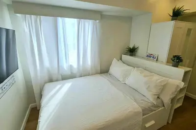 a small bedroom with a white bed with a window at California Themed Condo in BGC in Manila