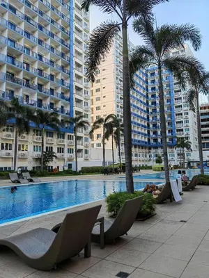a swimming pool with chairs and palm trees and buildings at Apartment By Douie At Sea Residences in Manila