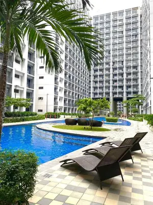 a swimming pool with two lounge chairs in front of a building at ClaySky Staycation S2T1-Cozy & Homey 1BR Apartment near MOA facing Pool with Own Parking with Netflix, HBO Max YouTube Premium & up to 200mbps Wifi in Manila