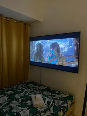 a flat screen tv hanging on a wall above a bed at Fame Residences Mandaluyong 1 Bedroom City View in Manila